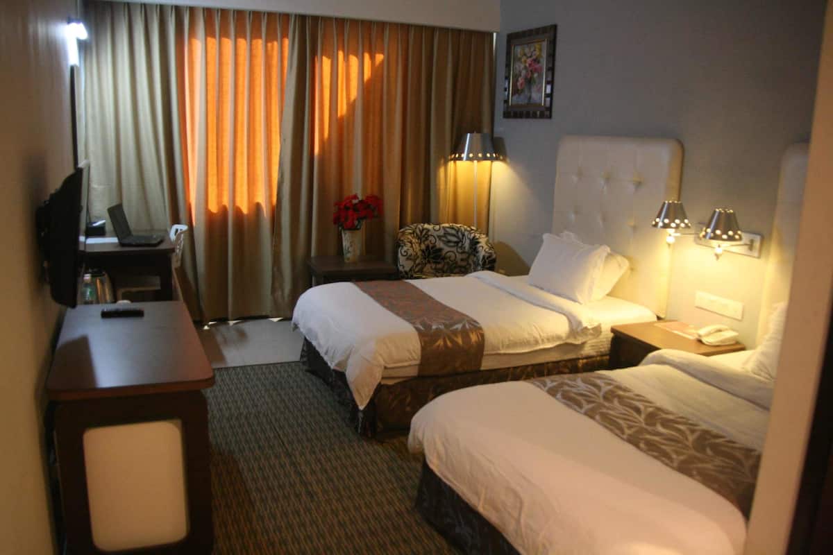 A hotel room with two beds, a desk, a chair, a lamp, and a painting on the wall.