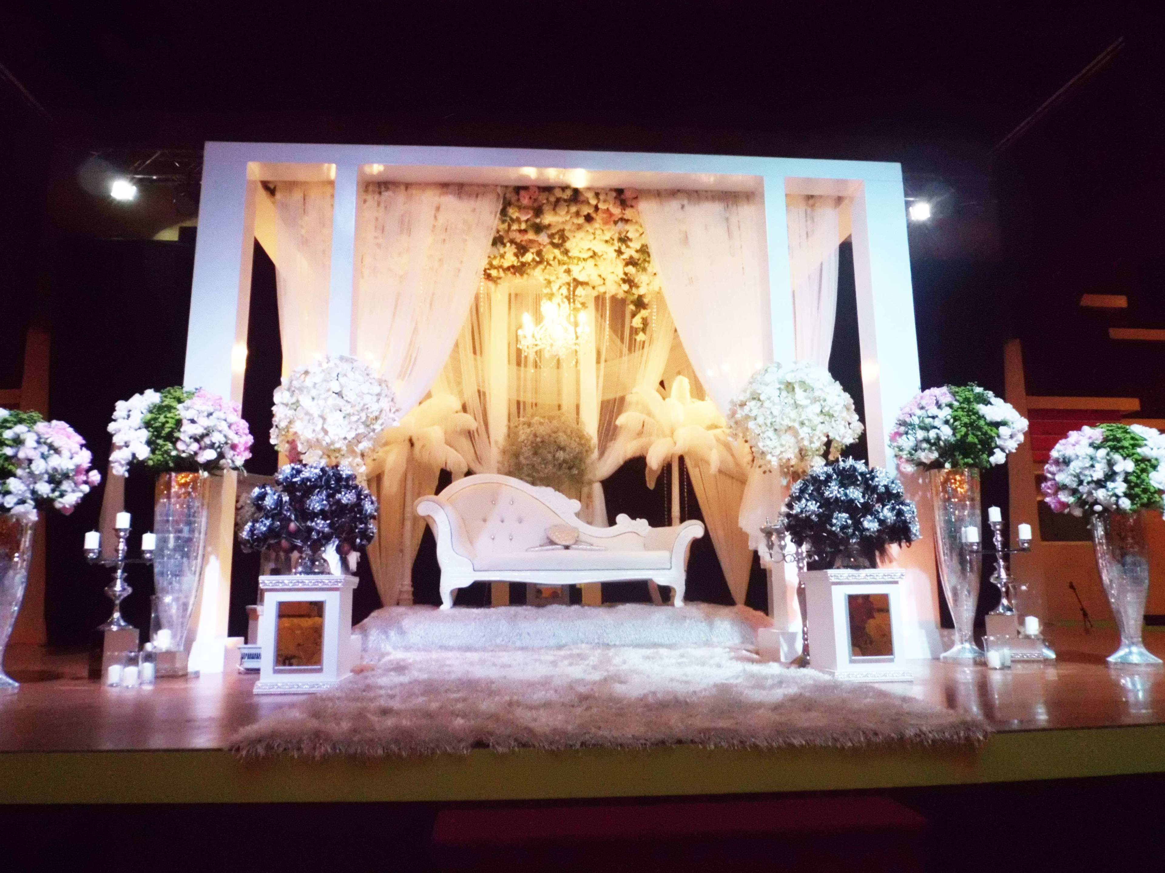 A stage with a white sofa, floral arrangements, and a chandelier.