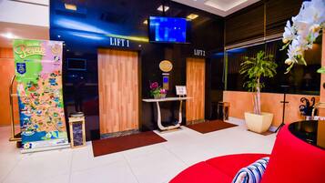 Welcome to our lobby, featuring a digital reception desk, two elevators, and a cozy seating area with a comfortable couch and round table.