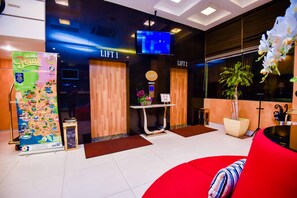 A hotel lobby with a reception desk, two lifts, a TV screen, a poster, and a red seating area. - Ritz Garden Hotel Manjung (Seri Manjung)