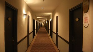Un couloir d’hôtel avec des portes des deux côtés, un sol recouvert de moquette et des luminaires fixés au mur.