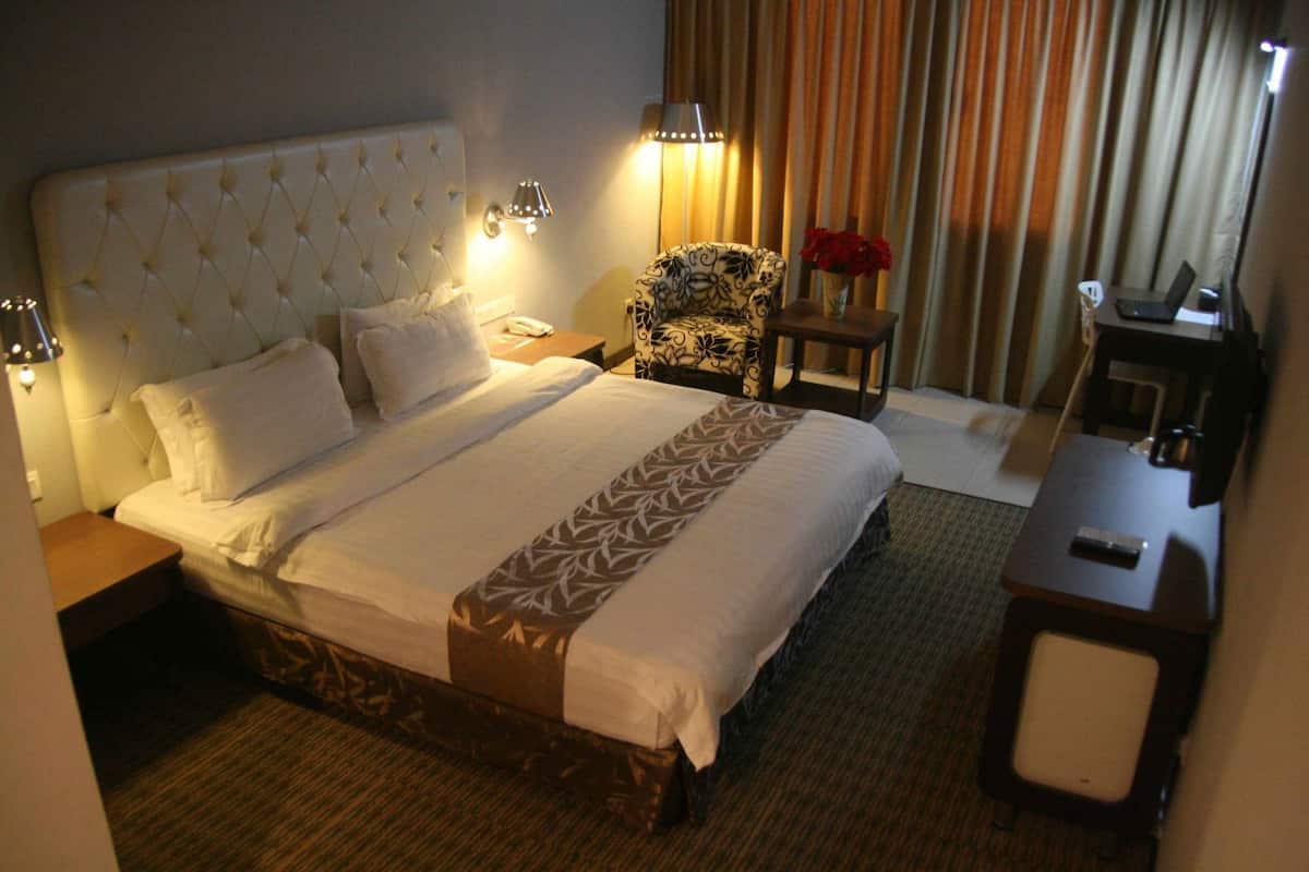 A hotel room with a large bed, a chair, a desk, and a lamp.