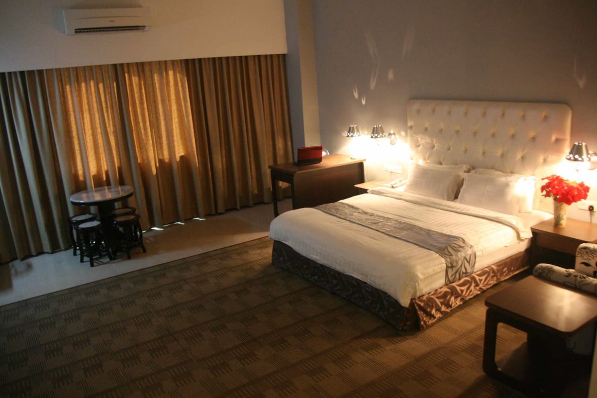 A hotel room with a large bed, bedside lamps, a small round table, and a chair.