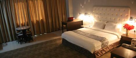 A hotel room with a large bed, bedside lamps, a small round table, and a chair.