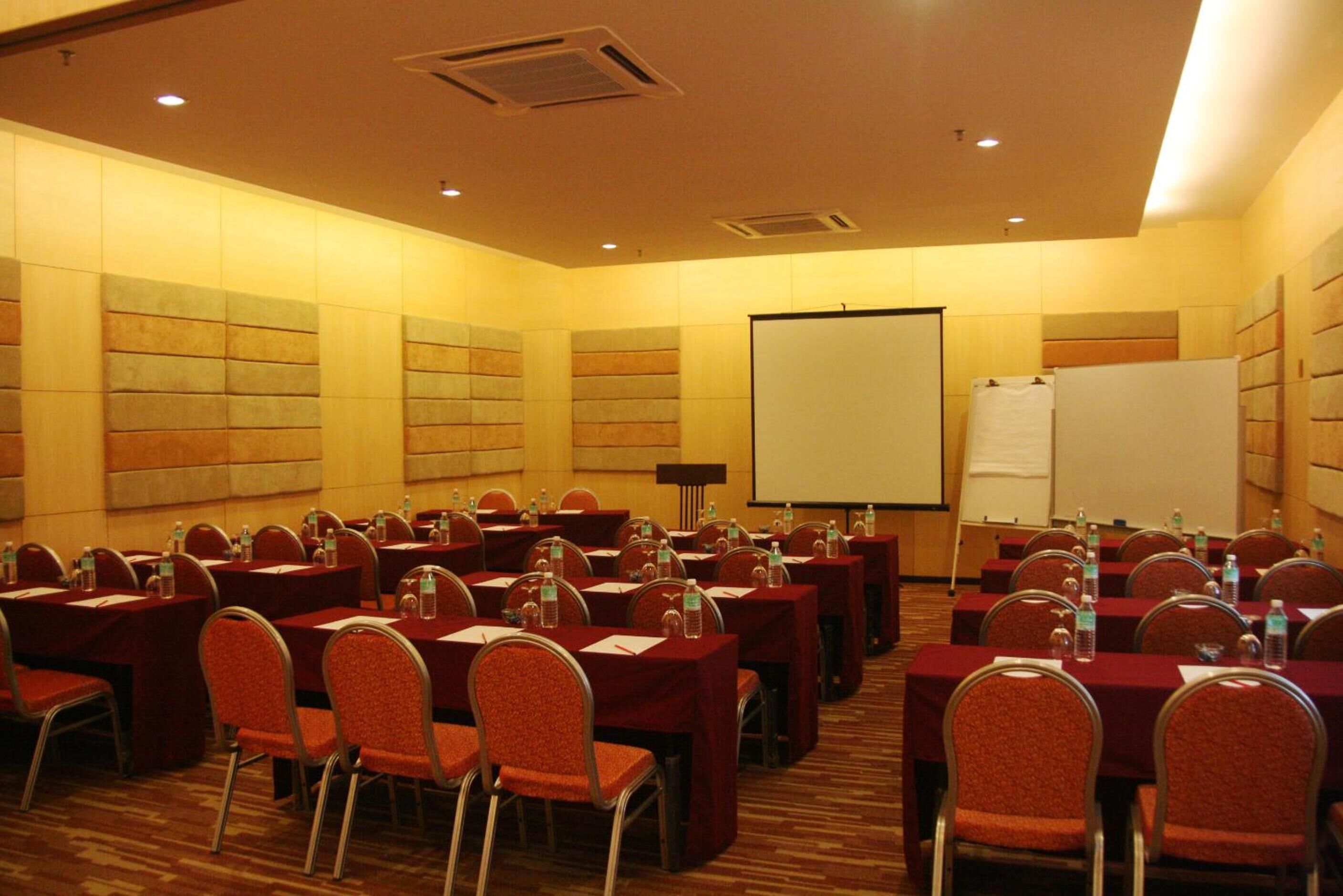 Un salón de conferencias con varias mesas y sillas, equipado con botellas de agua y documentos.