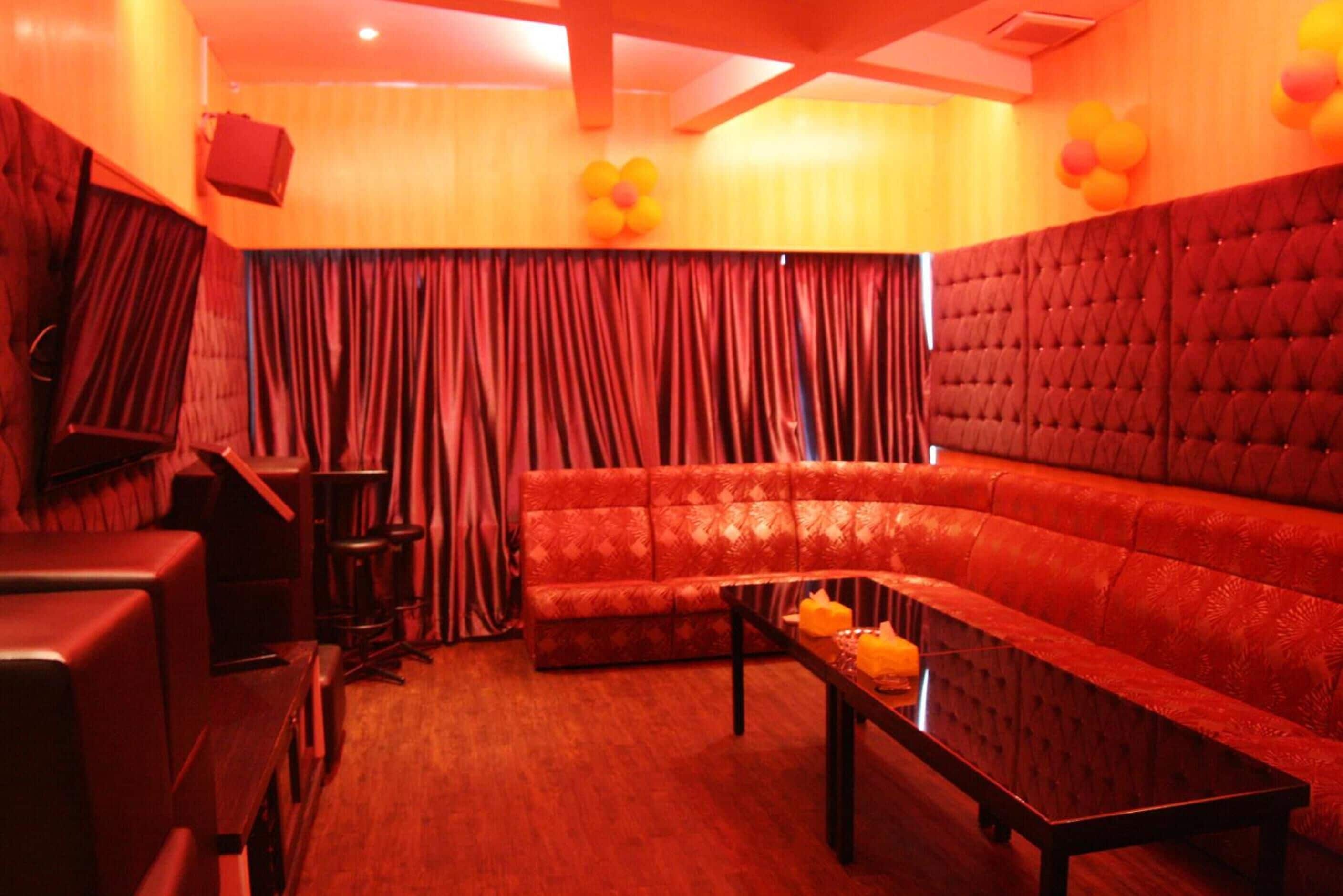 A room with a red upholstered sofa, a wooden coffee table, and a red curtain.