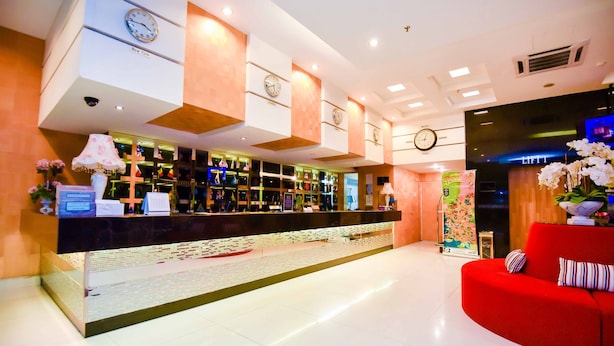 Un hall d’hôtel avec un comptoir d’accueil, un canapé rouge et des horloges accrochées aux murs.