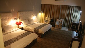 Une chambre d’hôtel avec deux lits, un coin salon avec un fauteuil, un bureau et une grande fenêtre avec des rideaux.