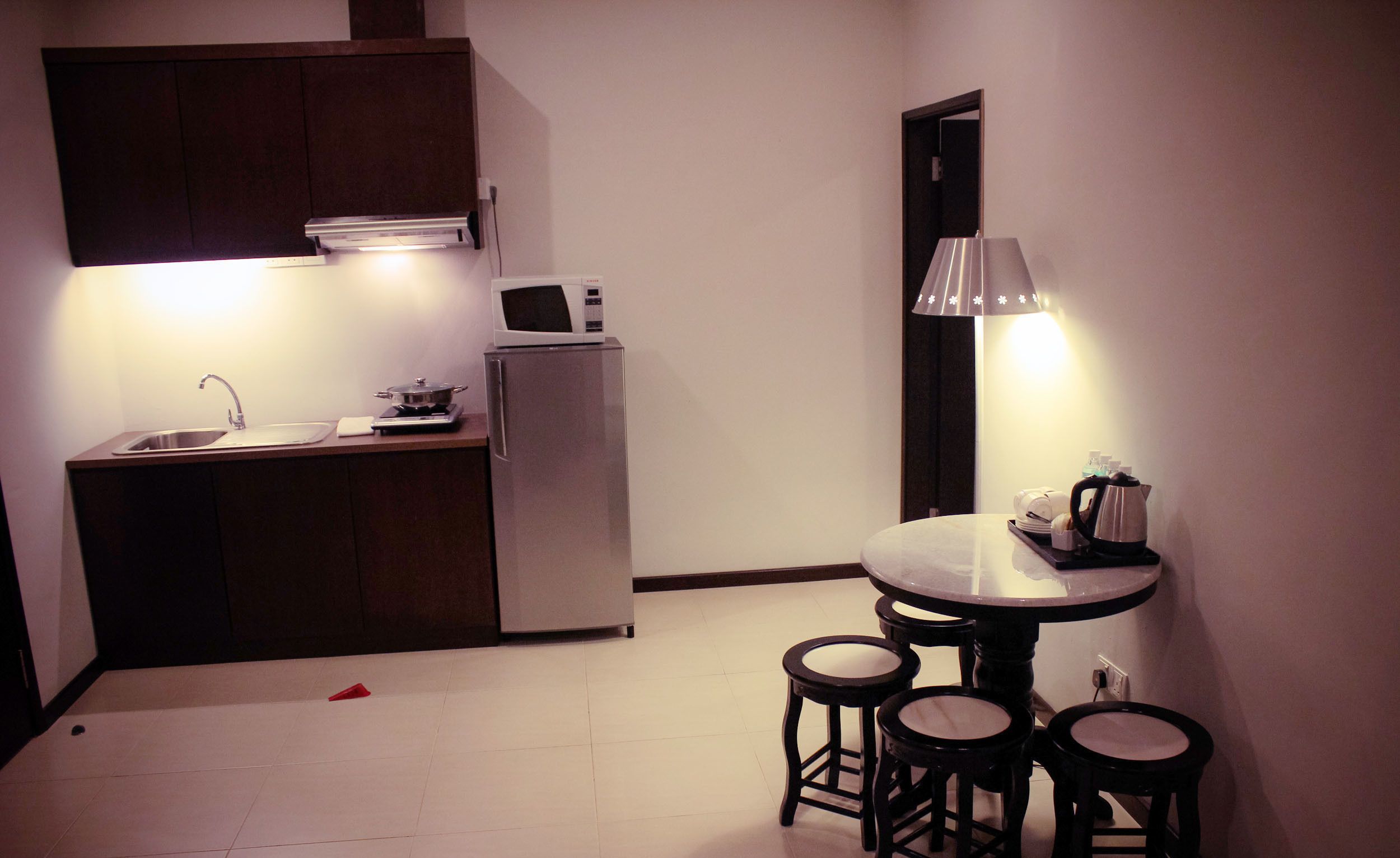 A compact kitchen with a sink, stove, and microwave. There are stools around a small table with a kettle.