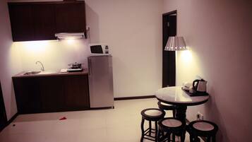 A compact kitchen with a sink, stove, and microwave. There are stools around a small table with a kettle.