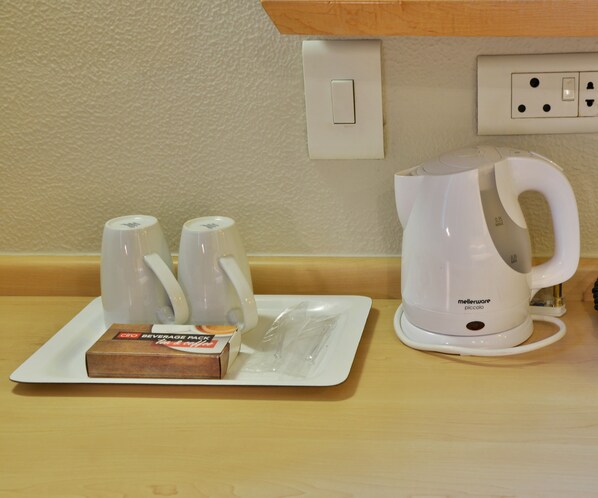 A kitchenette with a coffee maker, two mugs, and a beverage pack on a tray.