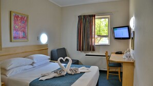 A hotel room with a bed, a desk, a chair, a TV, and a window with curtains.