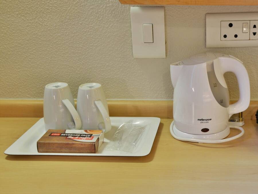 A kitchenette with a coffee maker, two mugs, and a beverage pack on a tray.