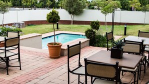 A patio area with a pool, outdoor seating, and a view of the surrounding greenery.