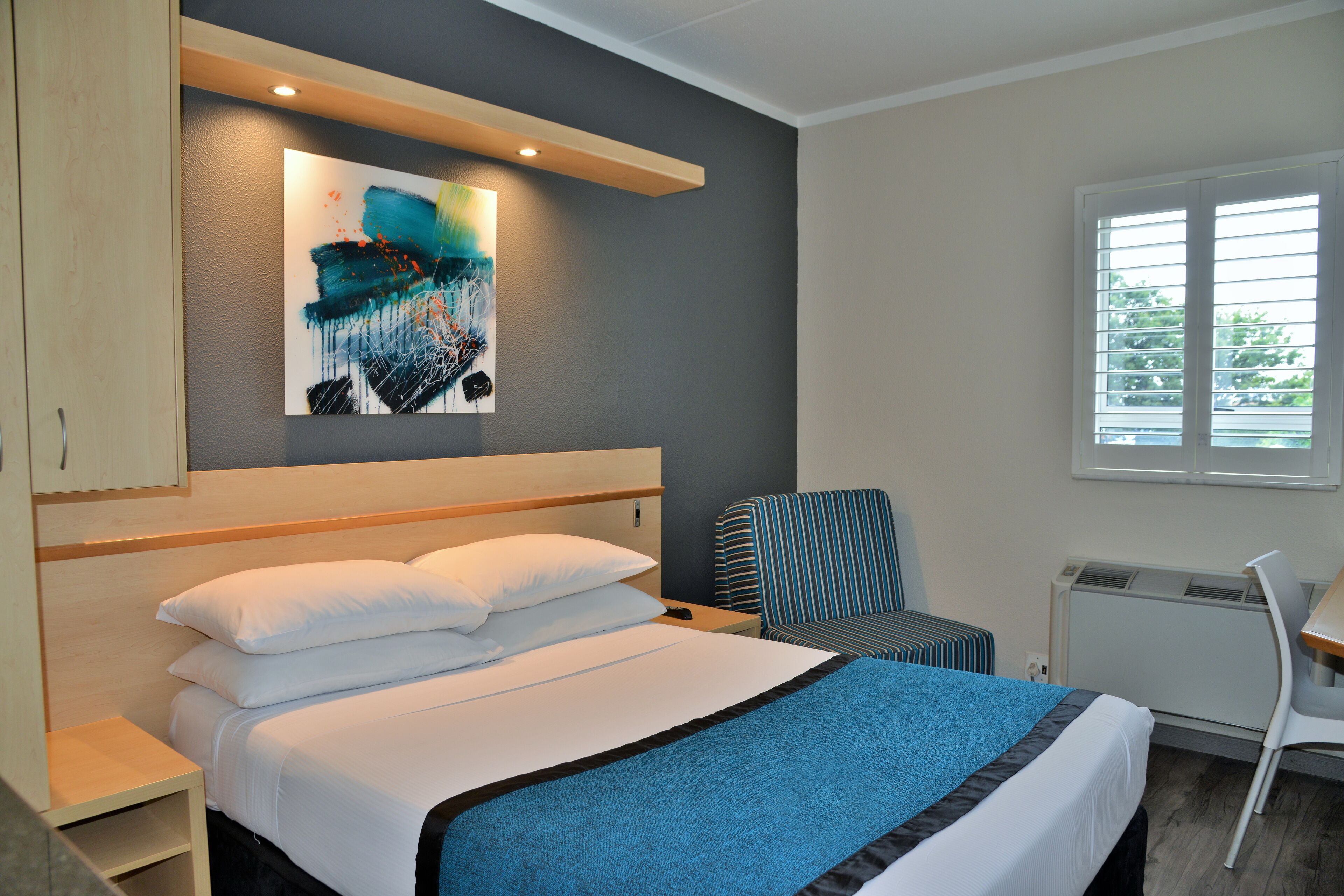 Une chambre moderne avec un grand lit, une chaise à rayures, un bureau et une fenêtre avec des stores.
