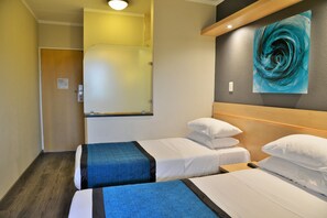 Une chambre d’hôtel avec deux lits, une tête de lit en bois, une grande peinture abstraite et un espace douche.