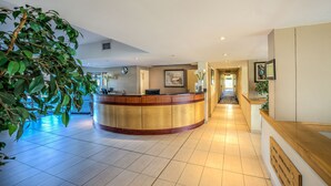A hotel reception area with a curved wooden reception desk, a tiled floor, and a large indoor plant on the left. - Road Lodge Richards Bay (Richards Bay)