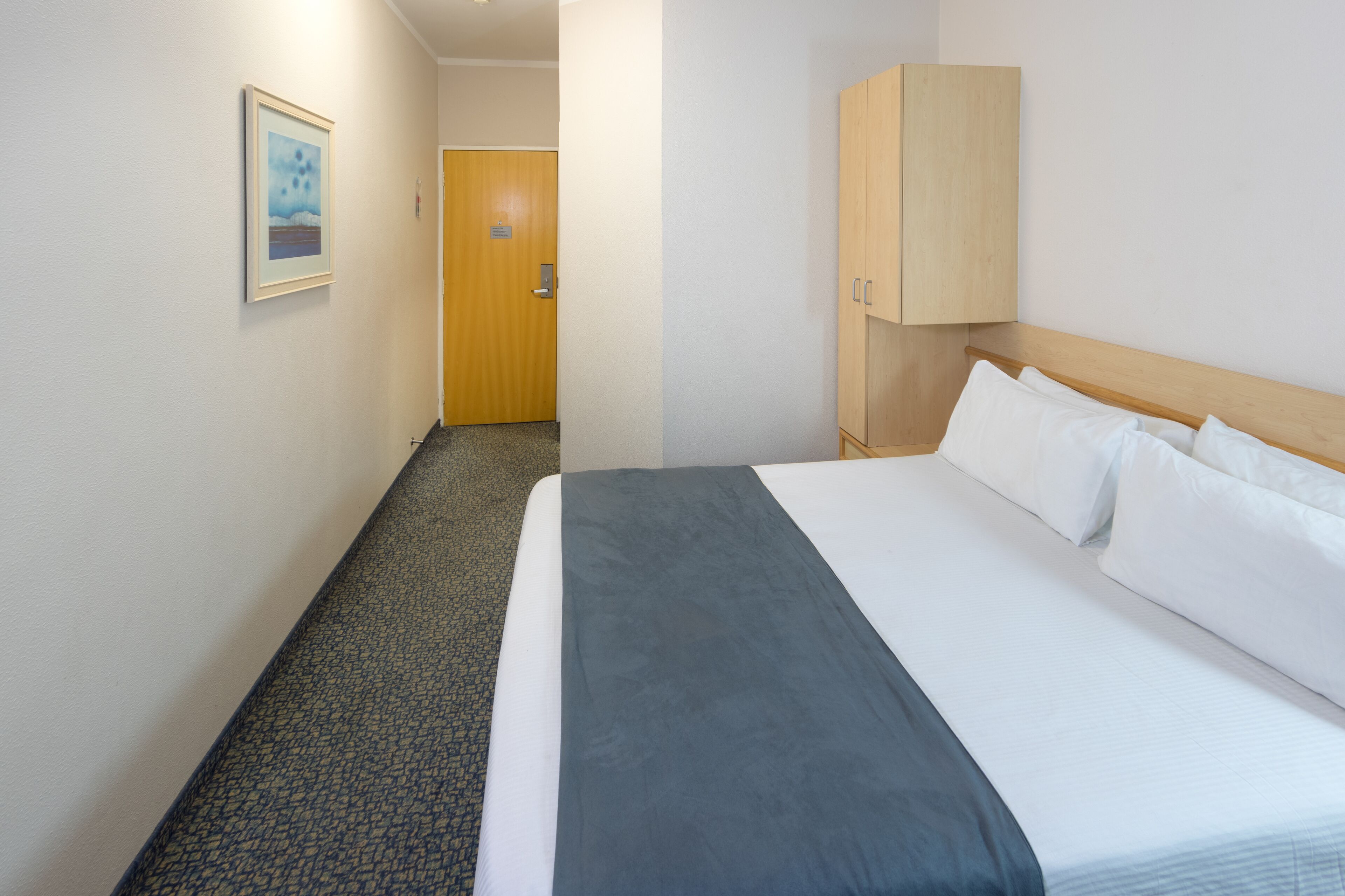 A hotel room with a bed, a wardrobe, a door, and a carpeted floor.