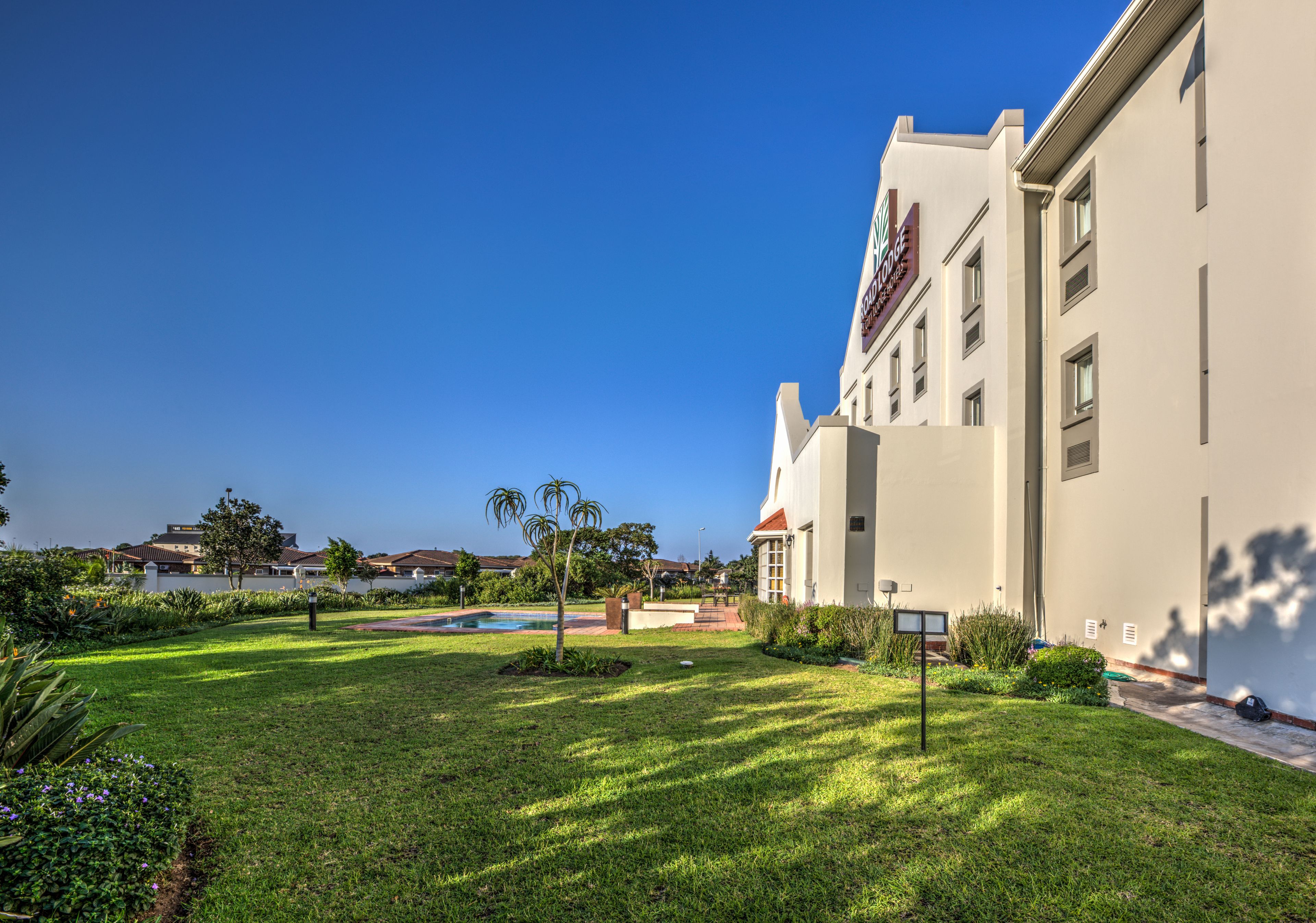 A hotel with a well-maintained lawn, a swimming pool, and a clear blue sky.