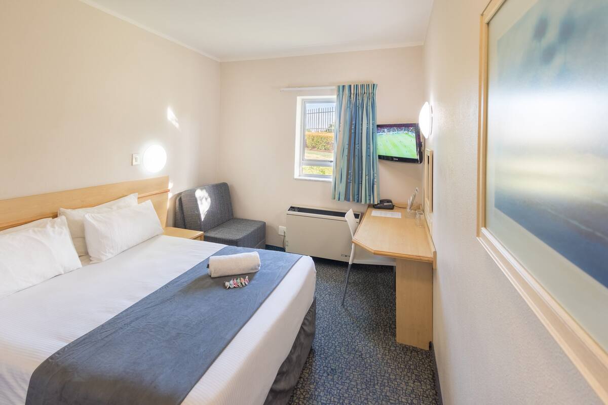 Ein Hotelzimmer mit Bett, Schreibtisch, Stuhl, Fernseher und einem Fenster mit Vorhängen.
