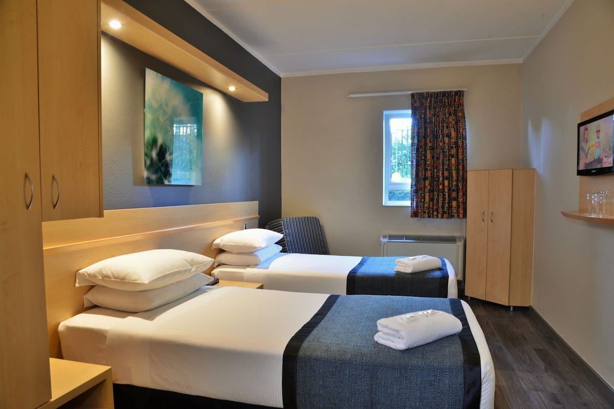 A hotel room with two beds, a window with curtains, a television, and a cabinet.