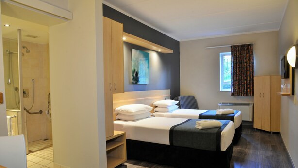 Une chambre d’hôtel avec deux lits, un espace douche et une fenêtre avec des rideaux.