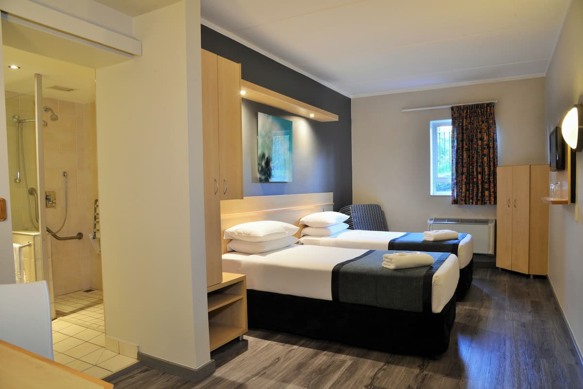 A hotel room with two beds, a shower area, and a window with curtains.