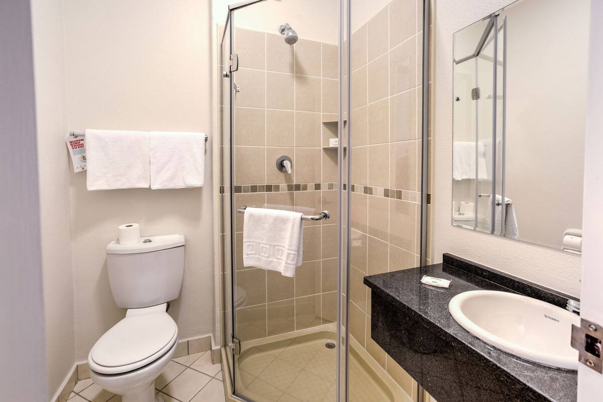 A bathroom with a toilet, a shower with a glass door, a sink, and a mirror.