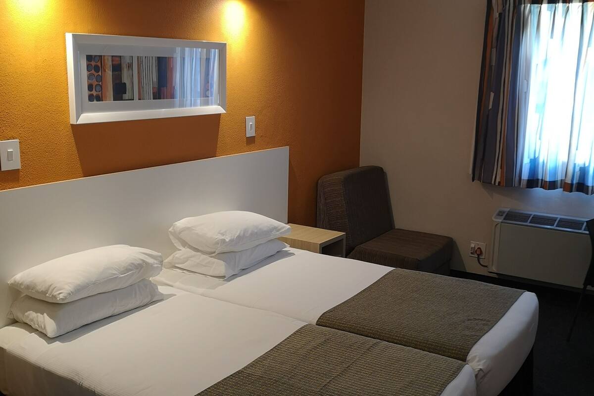 A hotel room with a large bed, a chair, a desk, and a window with curtains.