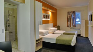 A hotel room with two beds, a shower, a small window with curtains, and a TV on the wall.