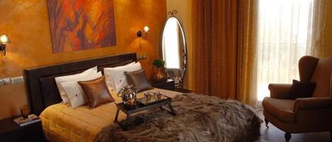 A bedroom with a large bed, a chair, a mirror, and a painting on the wall.