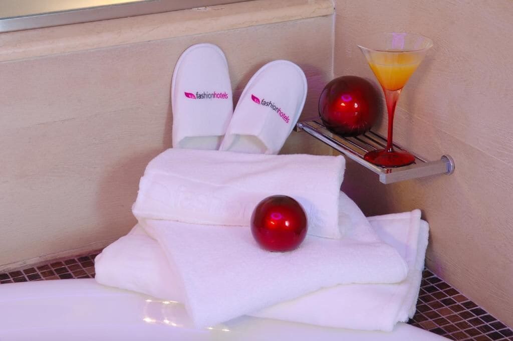 A bathroom with a towel rack holding white slippers and a martini glass with a red ornament.