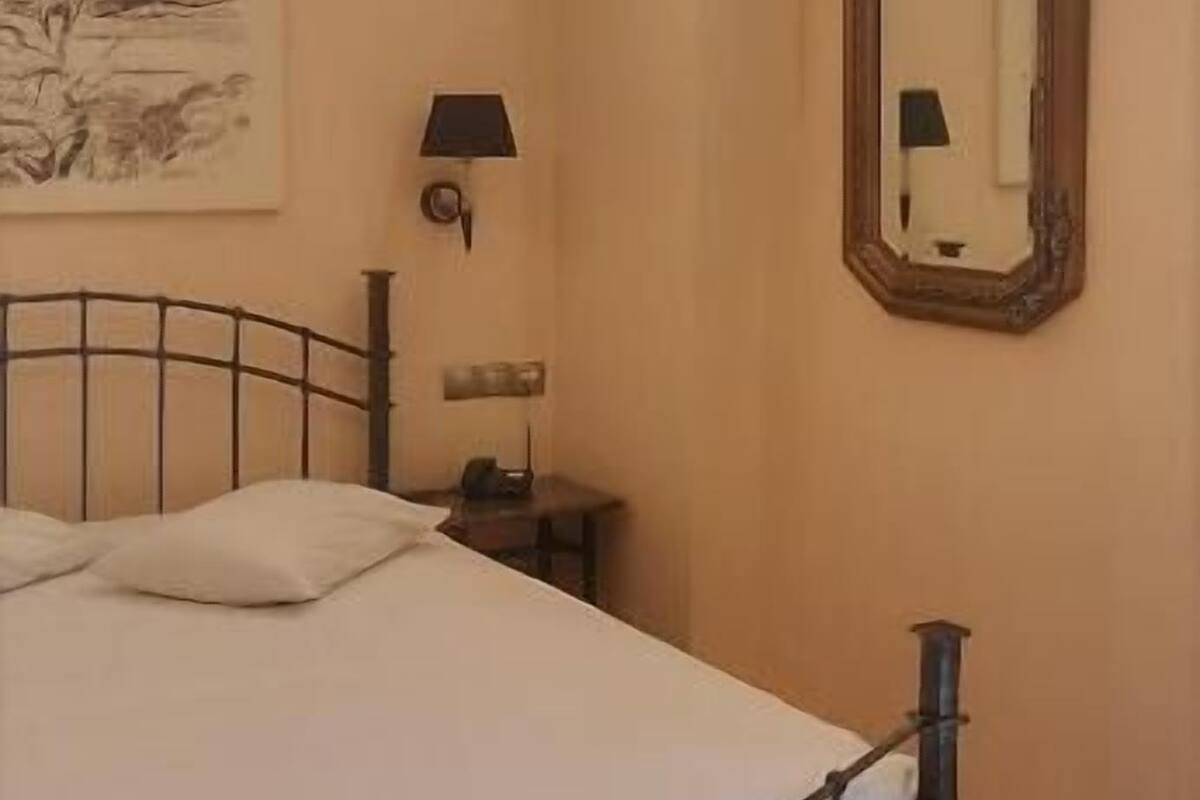 A bedroom with a bed, a nightstand, a lamp, a mirror, and a wall-mounted artwork.