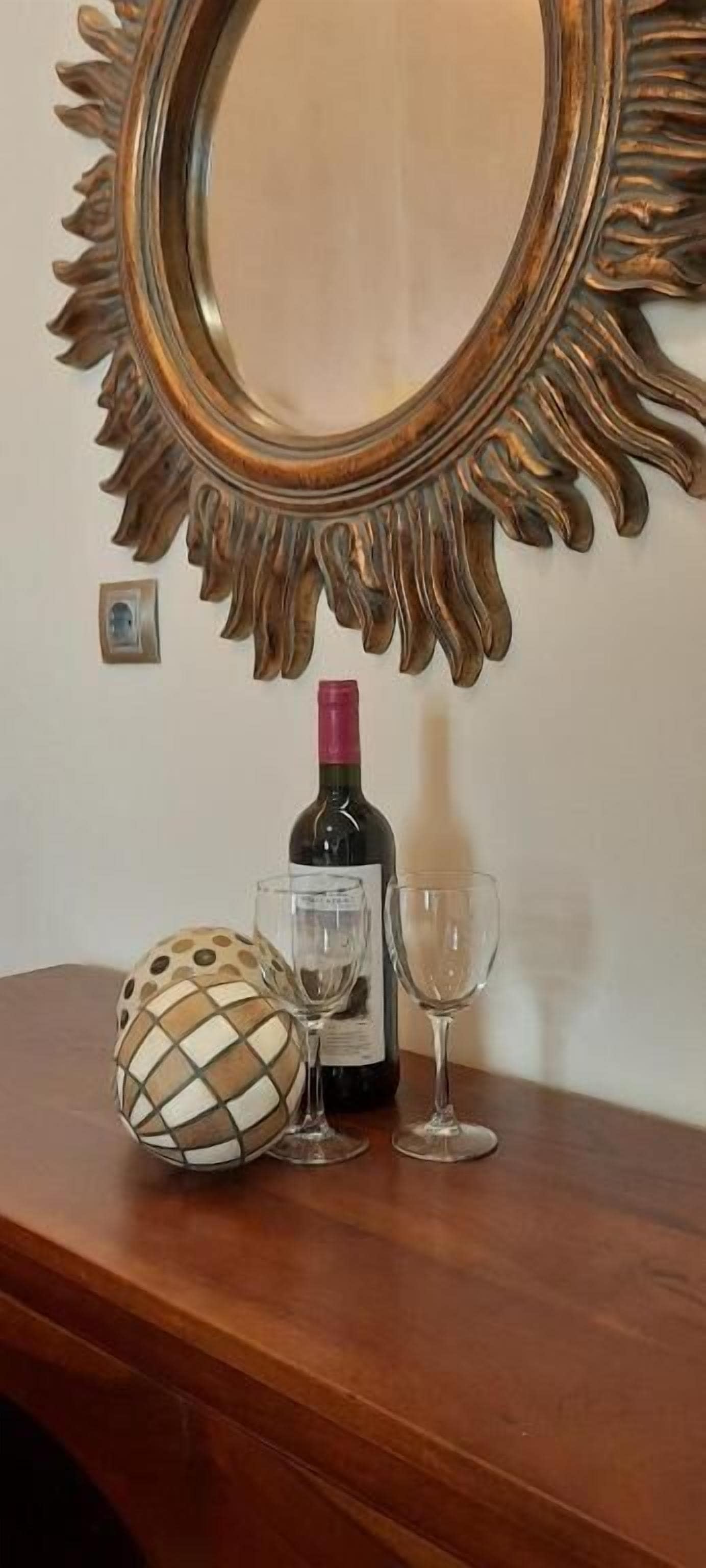 A wooden table with a decorative mirror, a wine bottle, and two wine glasses.