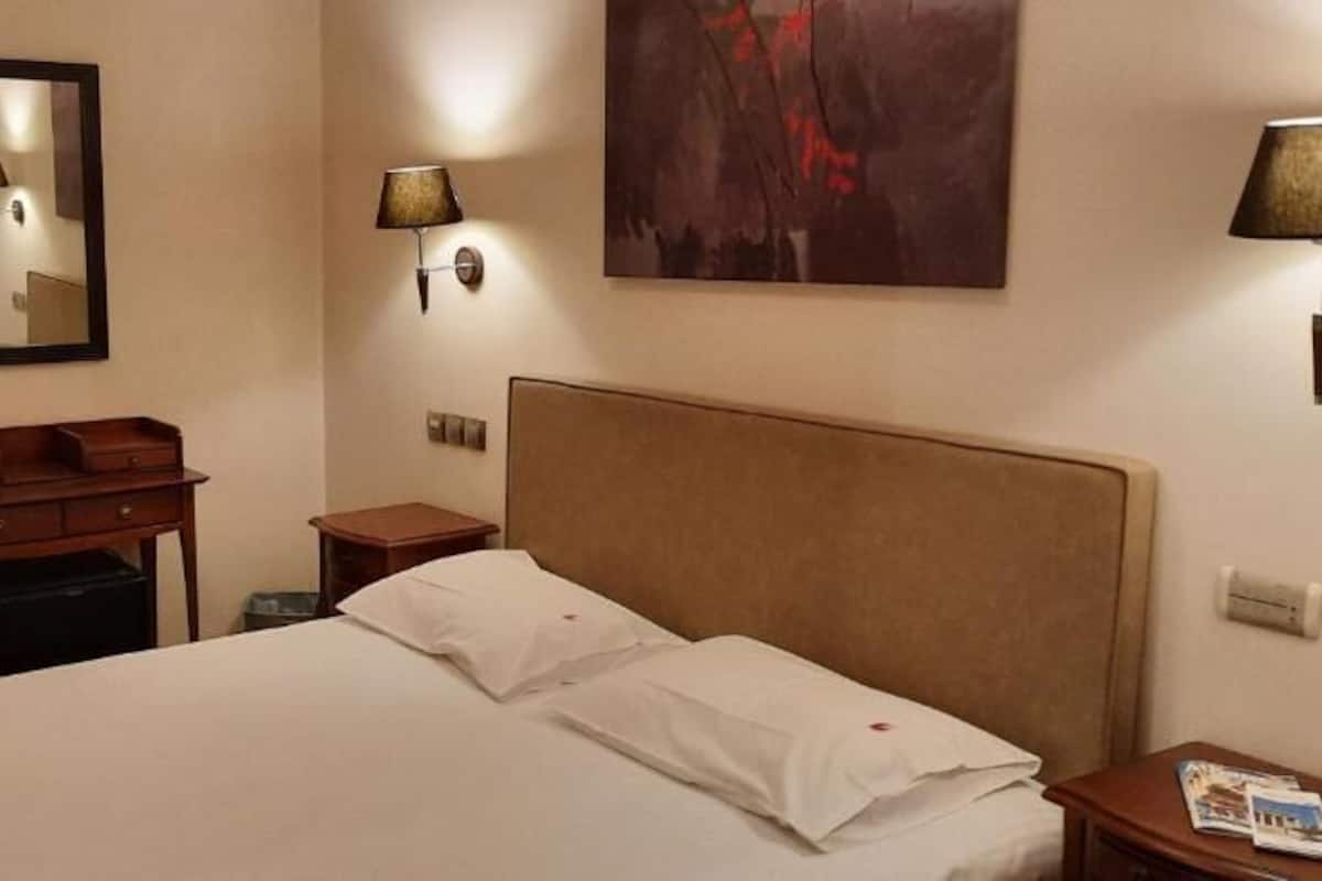 A hotel room with a bed, a nightstand, a lamp, a mirror, and a painting on the wall.
