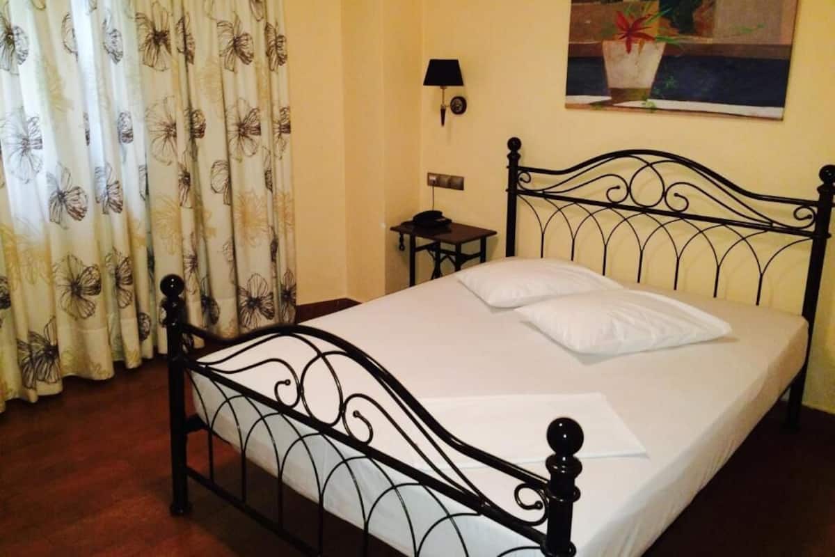 A bed with a metal frame, a small bedside table, a lamp, and a painting on the wall.