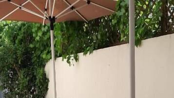 Un patio al aire libre con una mesa, sillas, una sombrilla grande y plantas en macetas.