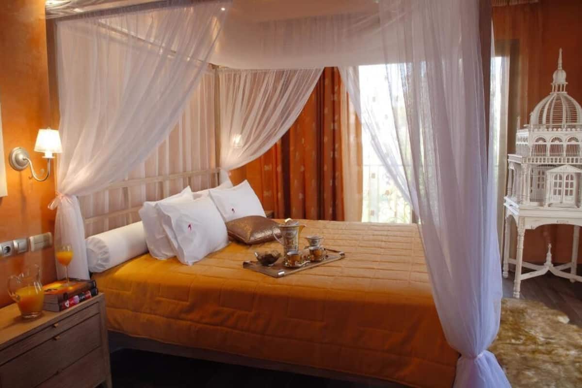A hotel room with a bed, a nightstand, a tray with tea and sugar, and a decorative birdcage.