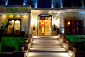A hotel entrance with a grand staircase, a reception desk, and a chandelier.