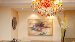 A reception desk with a chandelier, a clock, and a painting on the wall. - Olympic Fashion Hotels (Chalandri)