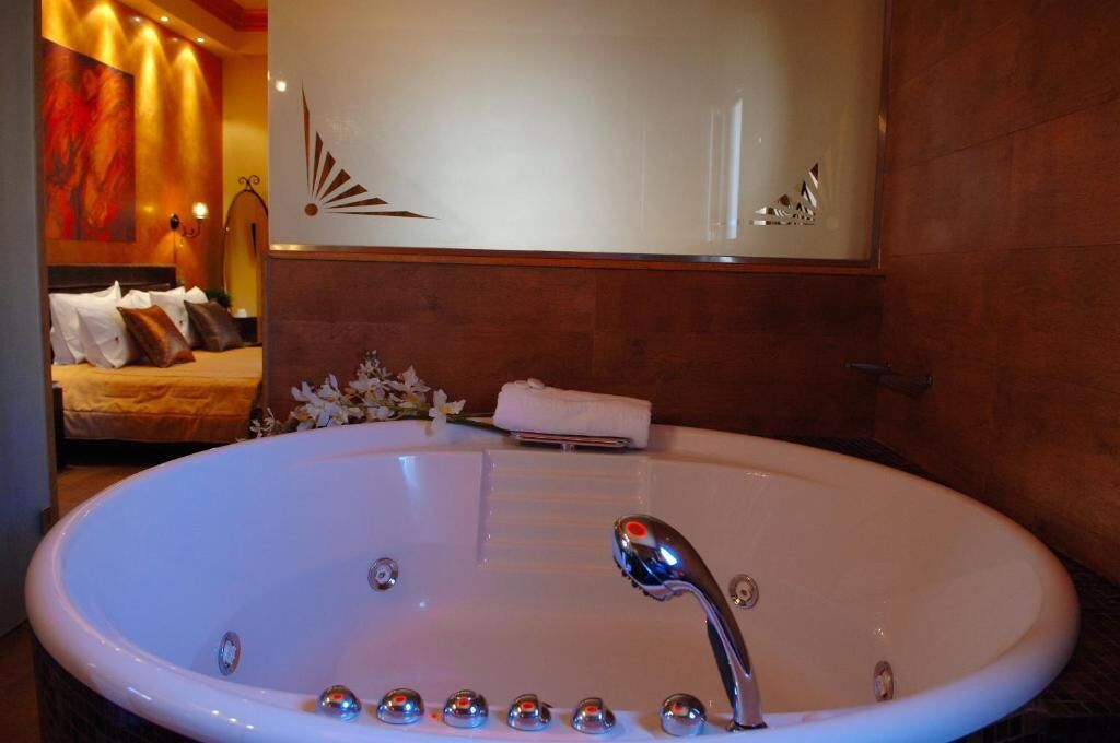 Una bañera ovalada grande con múltiples jets, un espejo encima y una cama con almohadones al fondo.