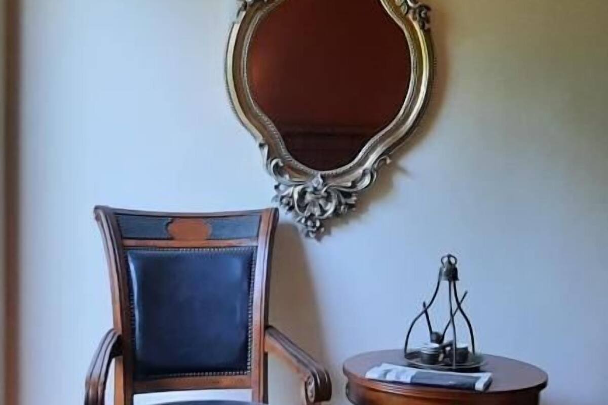 A chair with a cushioned seat and backrest, a round table with a base, and a decorative mirror on the wall.