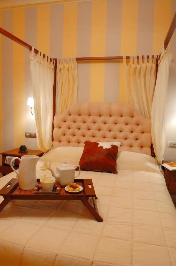 A bedroom with a tufted headboard, a bed with white and red bedding, a tray with breakfast items, and striped curtains.