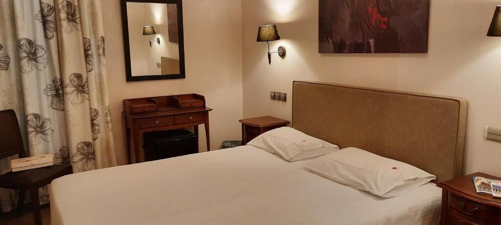 A hotel room with a large bed, a desk with a lamp, a dresser, and a mirror on the wall.