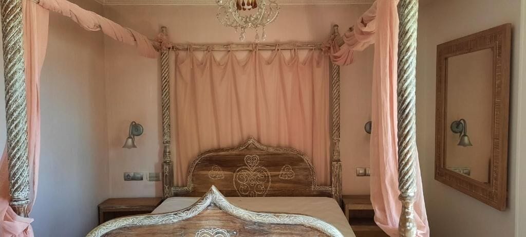 Een slaapkamer met een hemelbed, een kroonluchter en een spiegel aan de muur.