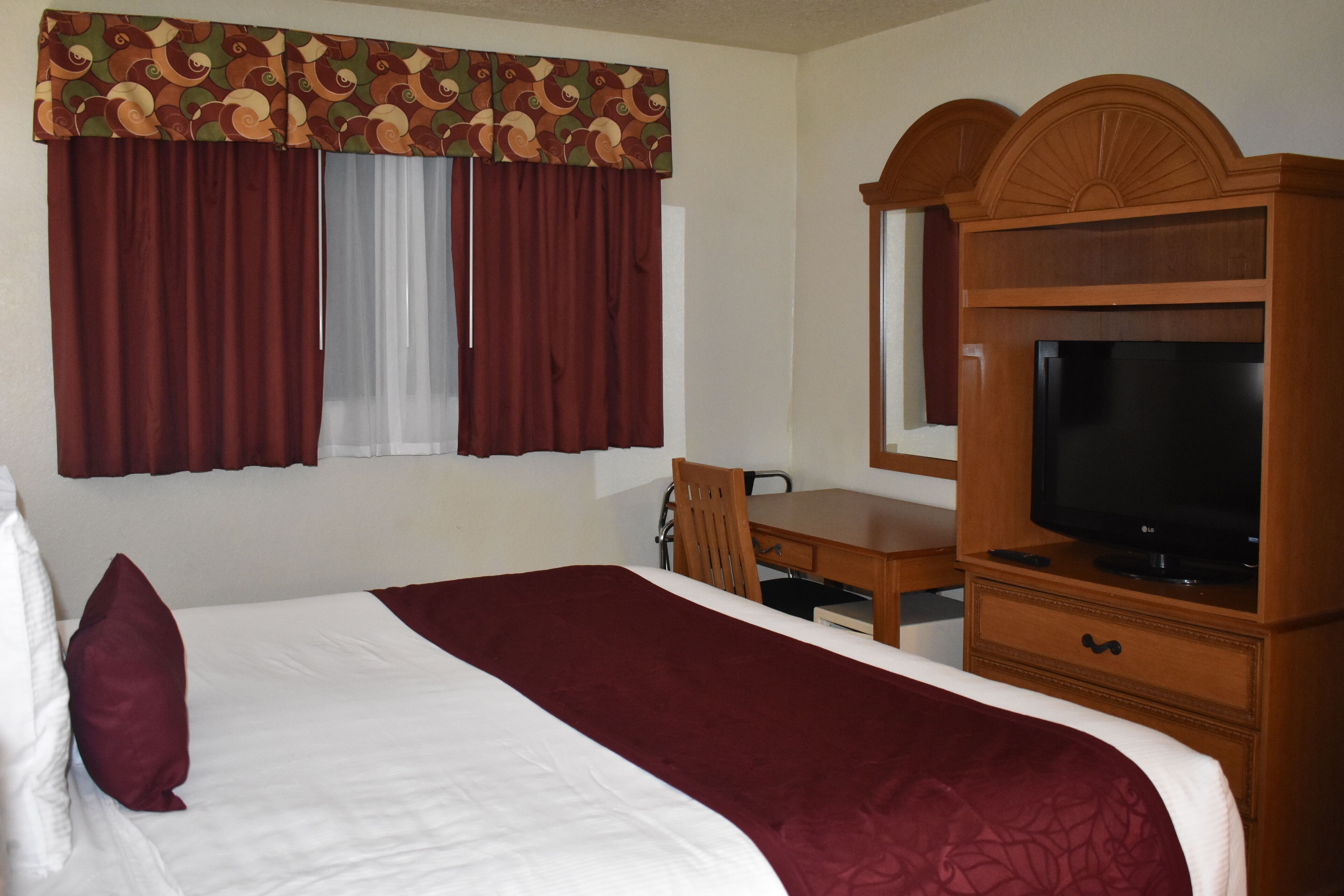 Een hotelkamer met een groot bed, een bureau, een televisie en een raam met gordijnen.