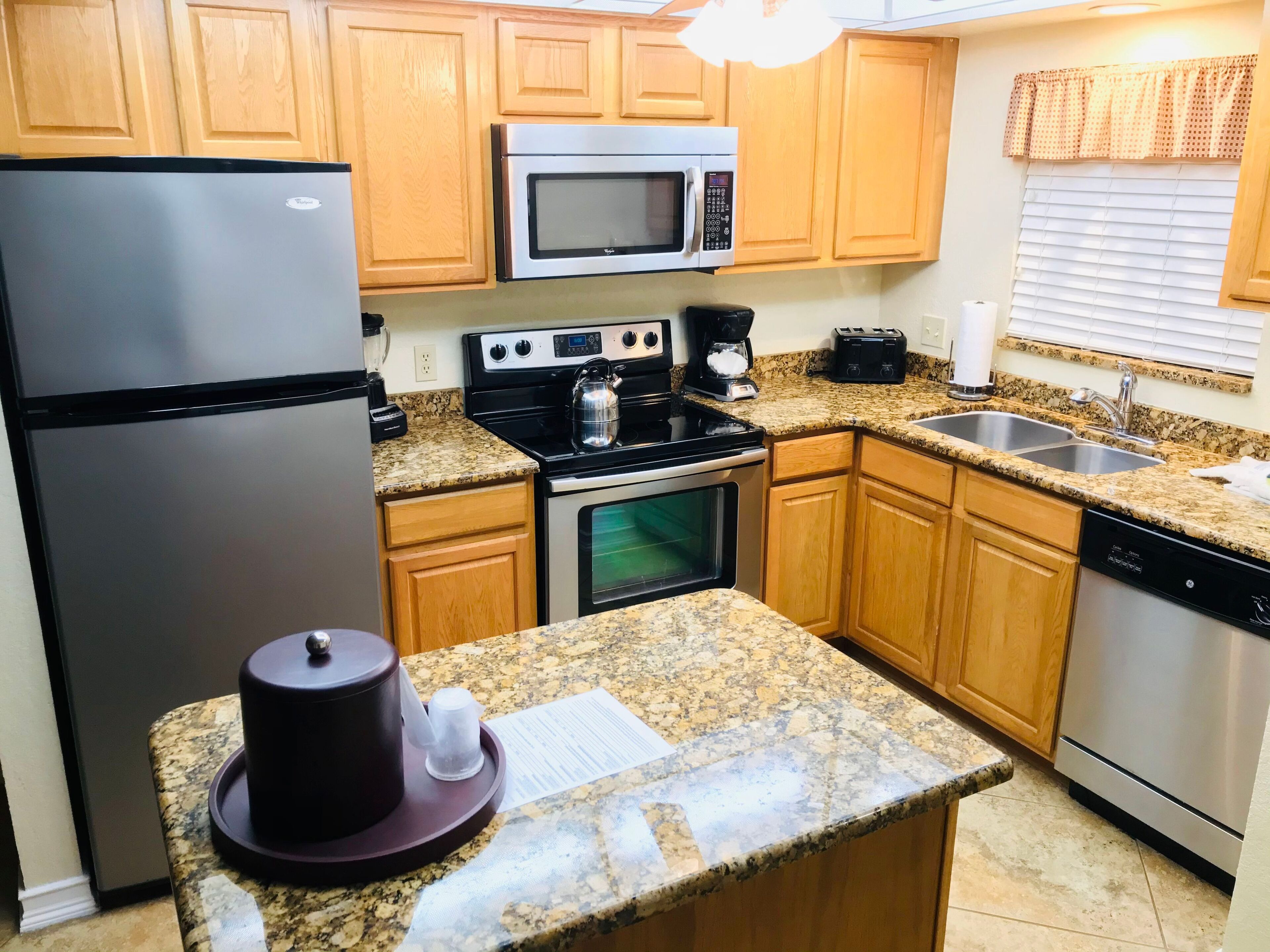 A kitchen with wooden cabinets, a stainless steel refrigerator, a microwave, a stove, an oven, a sink, and a dishwasher.