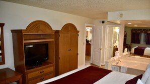 A hotel room with a large bed, a television, a wardrobe, a bathroom with a bathtub, and a kitchenette. - Club Sevilla (Kissimmee)