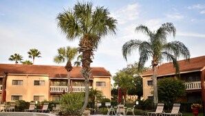 A pool area with lounge chairs and palm trees, surrounded by a building with a tiled roof. - Club Sevilla (Kissimmee)