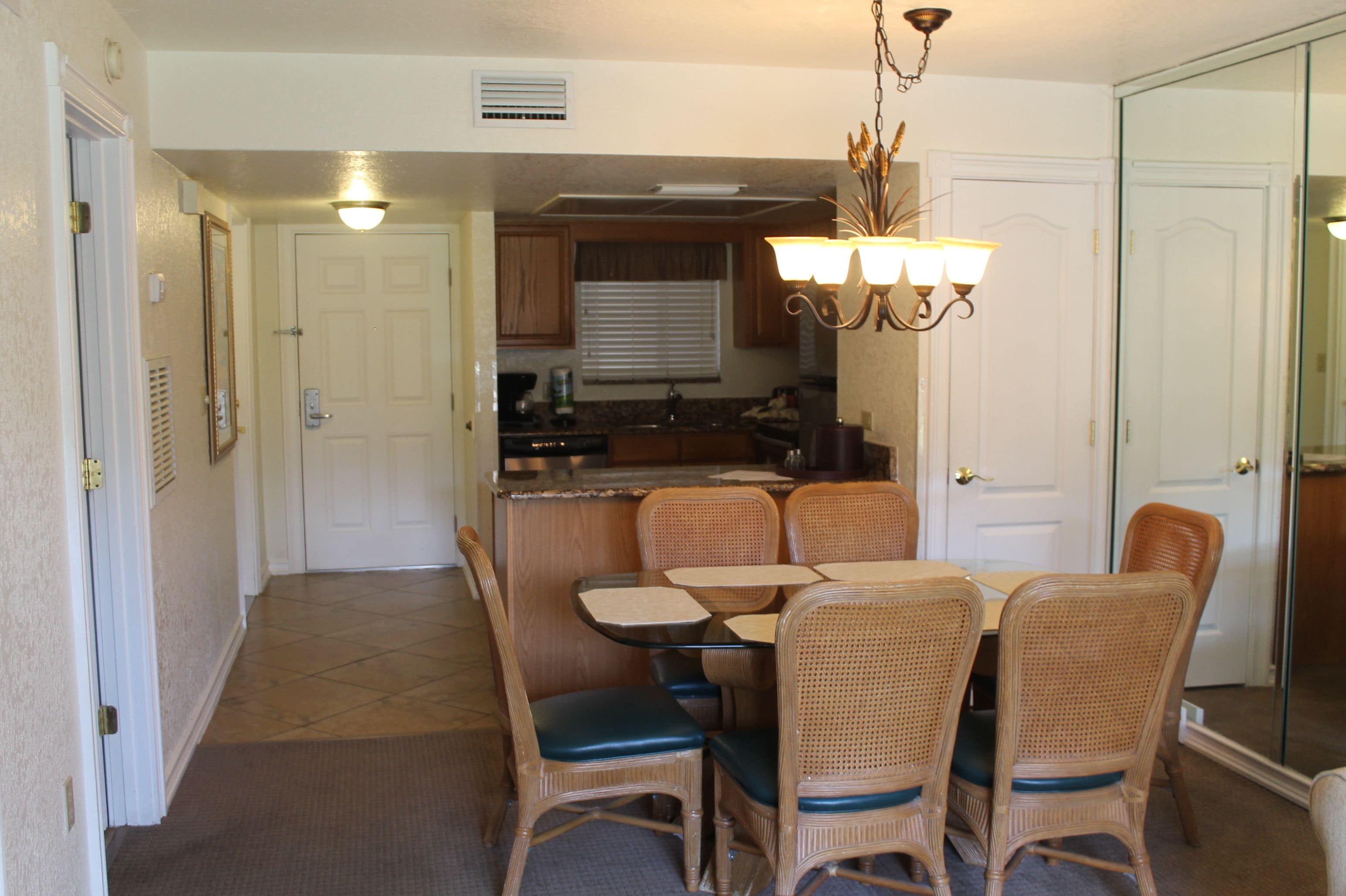 A dining area with wicker chairs and a table, a kitchen with wooden cabinets, and a hallway with a door.